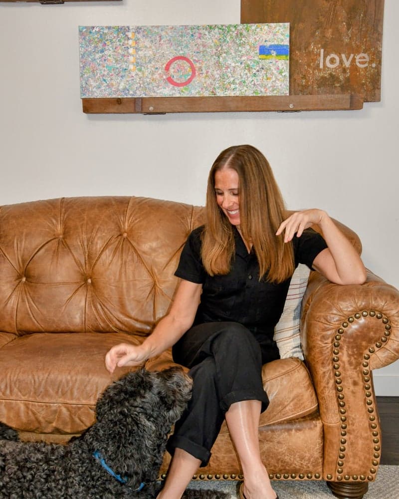 Monica sitting on a leather couch with her dog